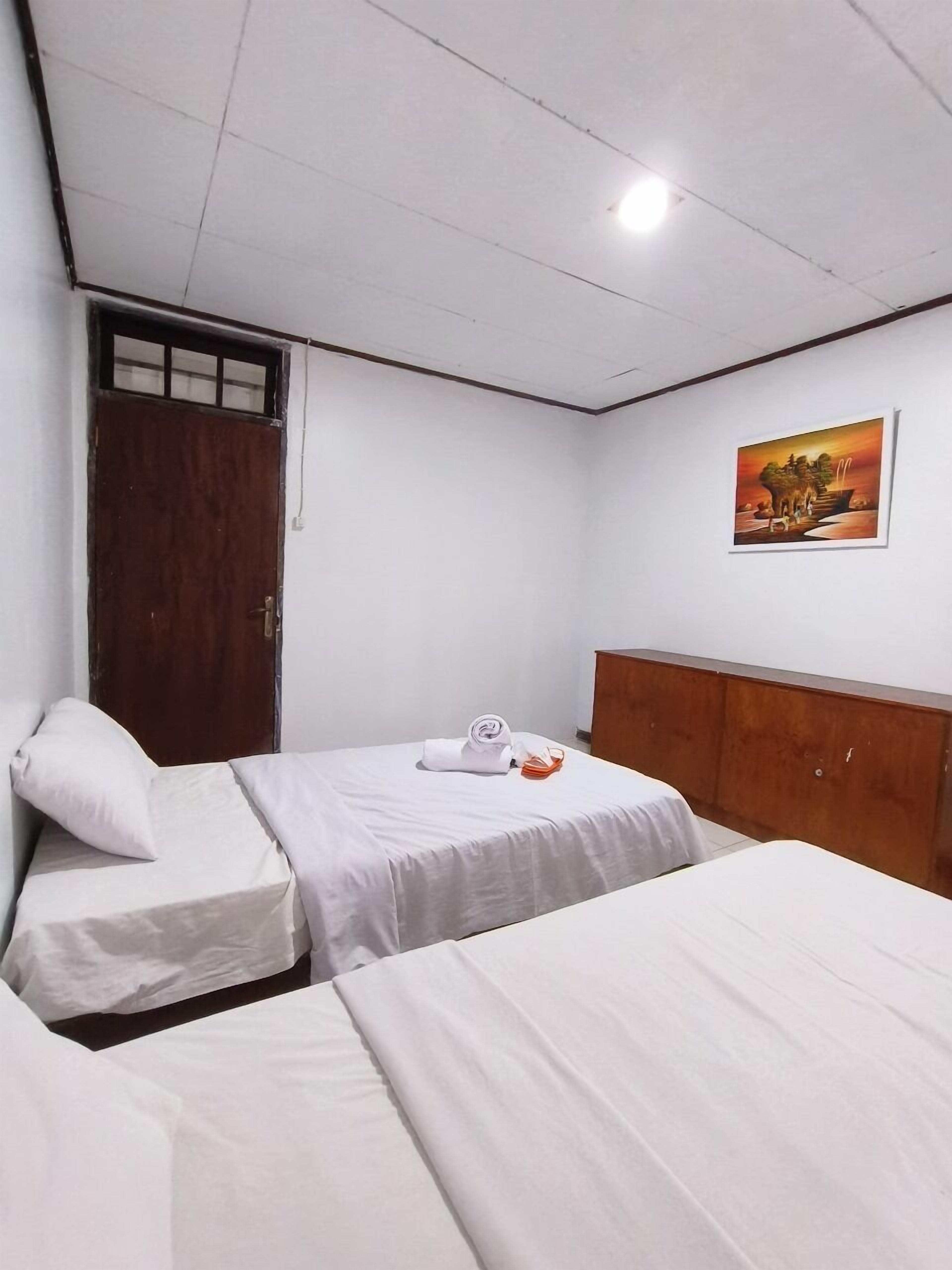Habitación de hotel con dos camas, un armario de madera, un cuadro en la pared y una puerta con ventanal.