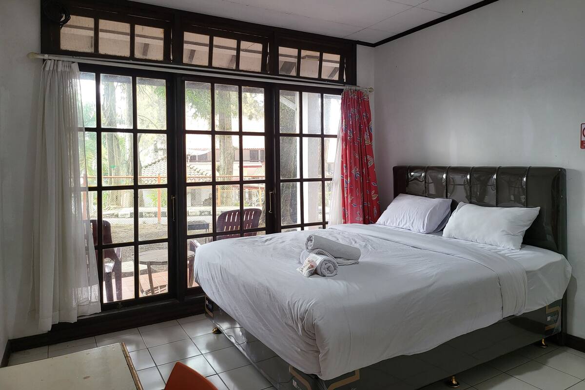 A hotel room with a large window, a bed with white linens, and a view of the outside.