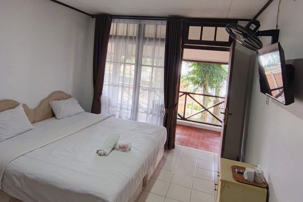 A hotel room with a bed, a TV, a fan, and a small table with cups.
