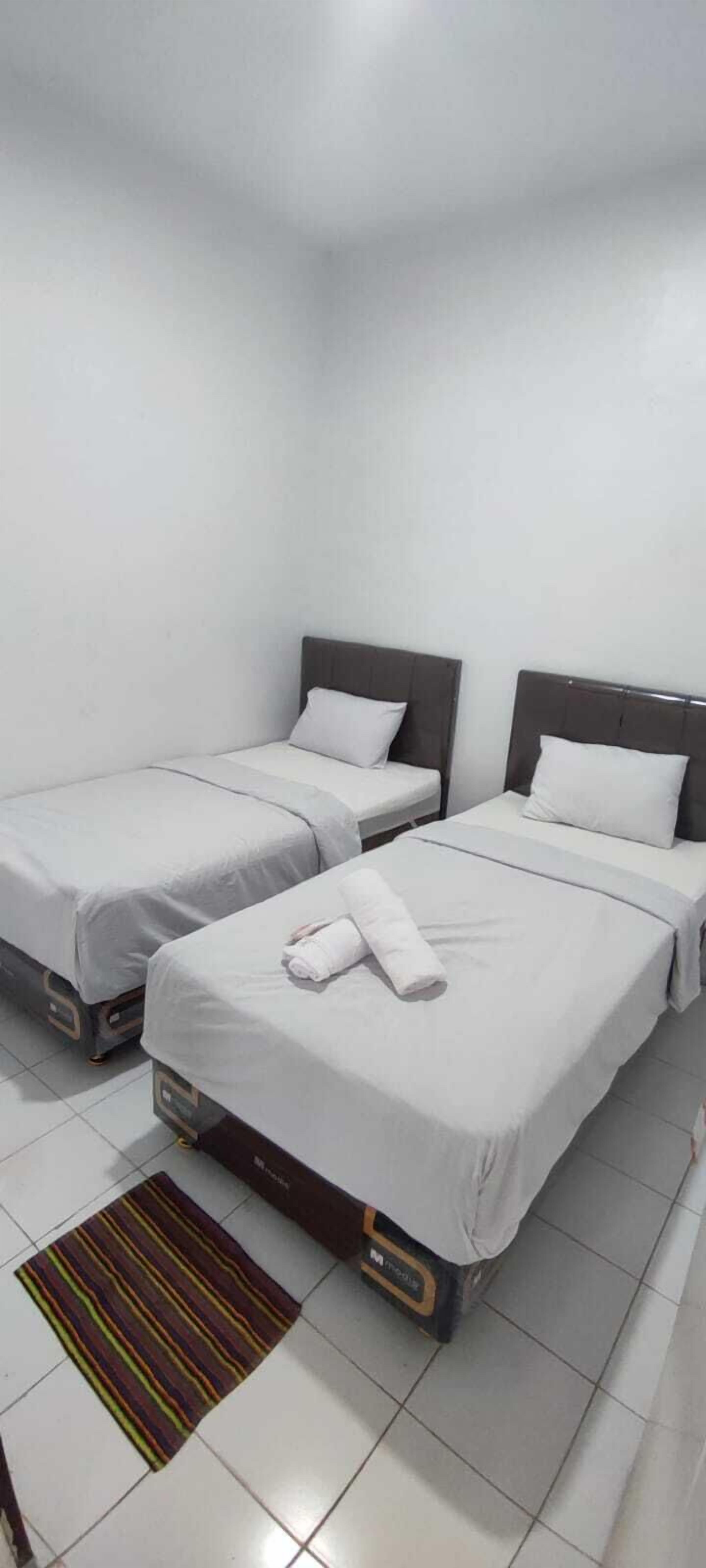 A hotel room with two single beds, a small table, and a striped rug.