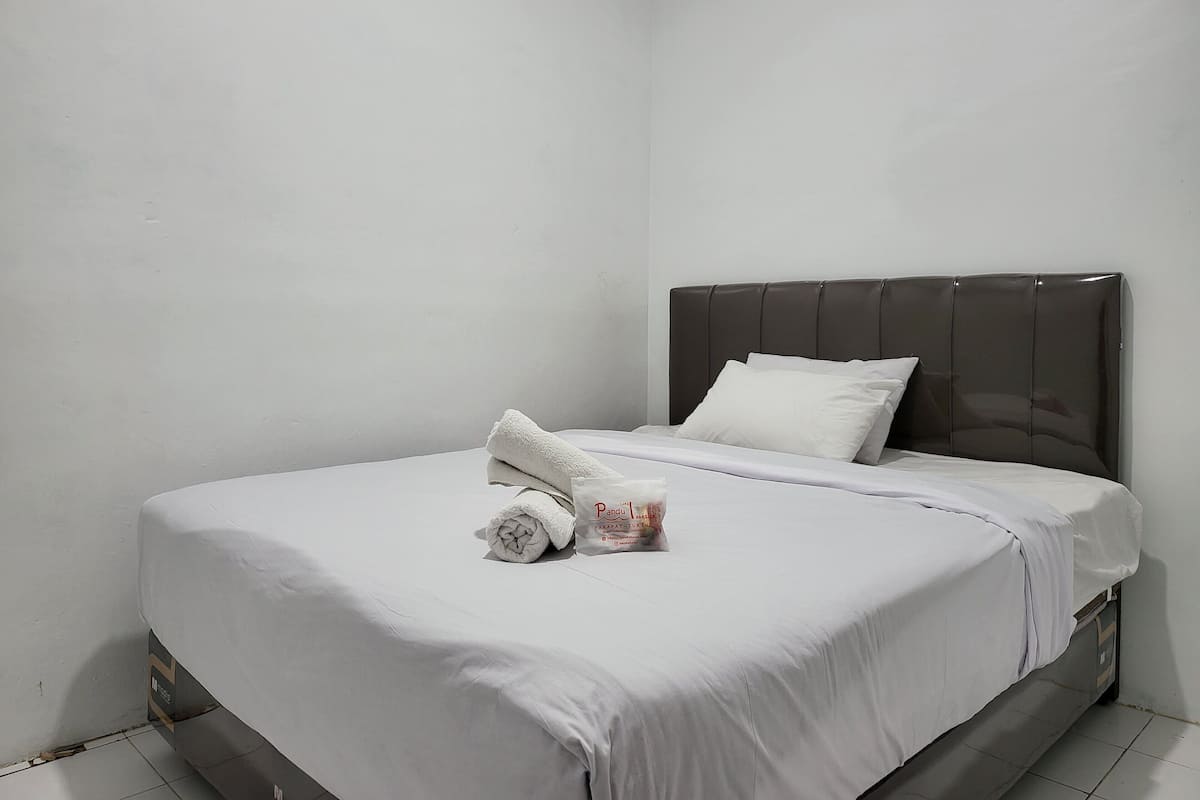 A neatly made bed with white linens, a rolled towel, and a small bottle of lotion on the bed.