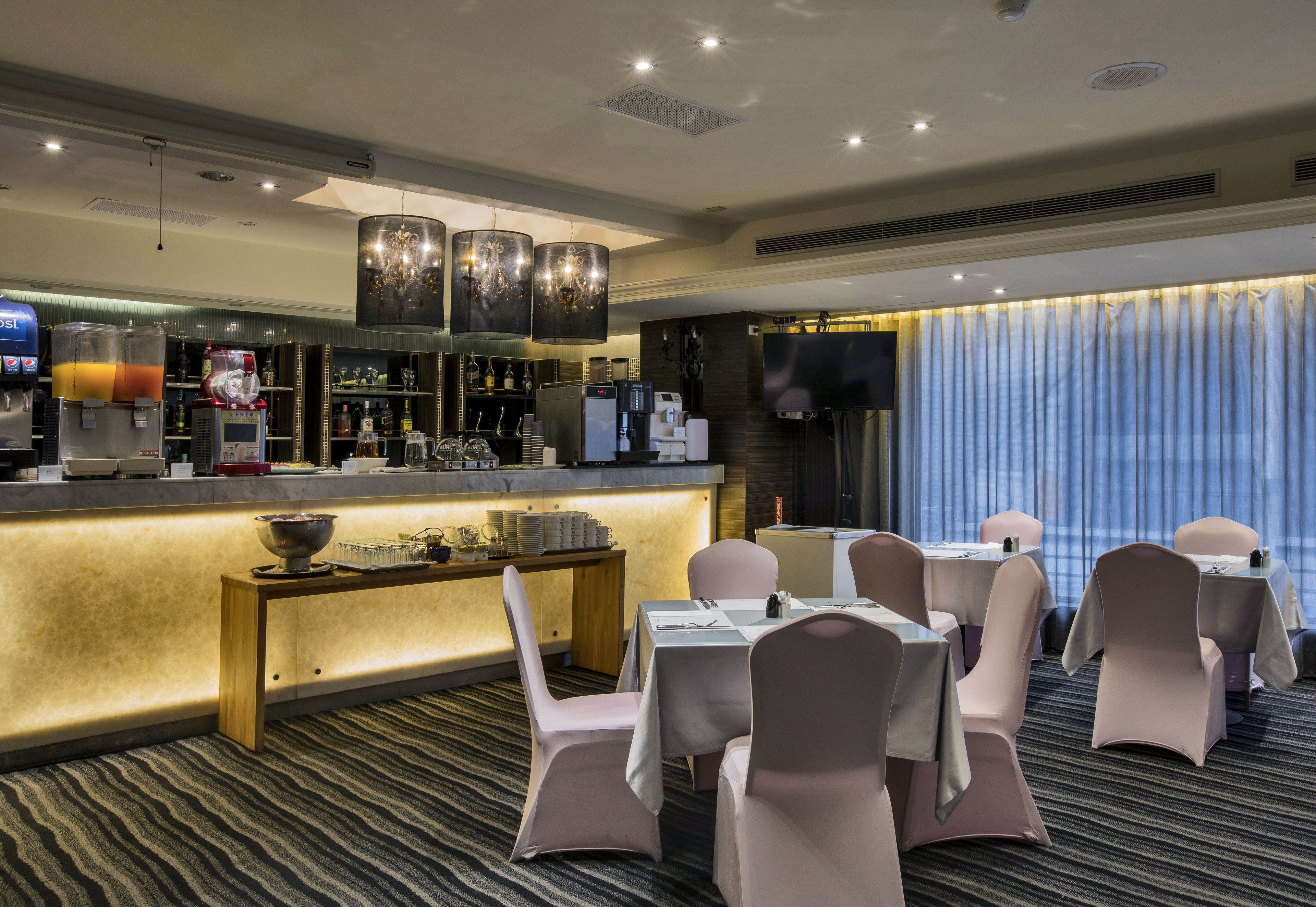 Ein Hotel-Speisesaal mit Bar, Tischen, Stühlen und einem großen Fenster mit Vorhängen.