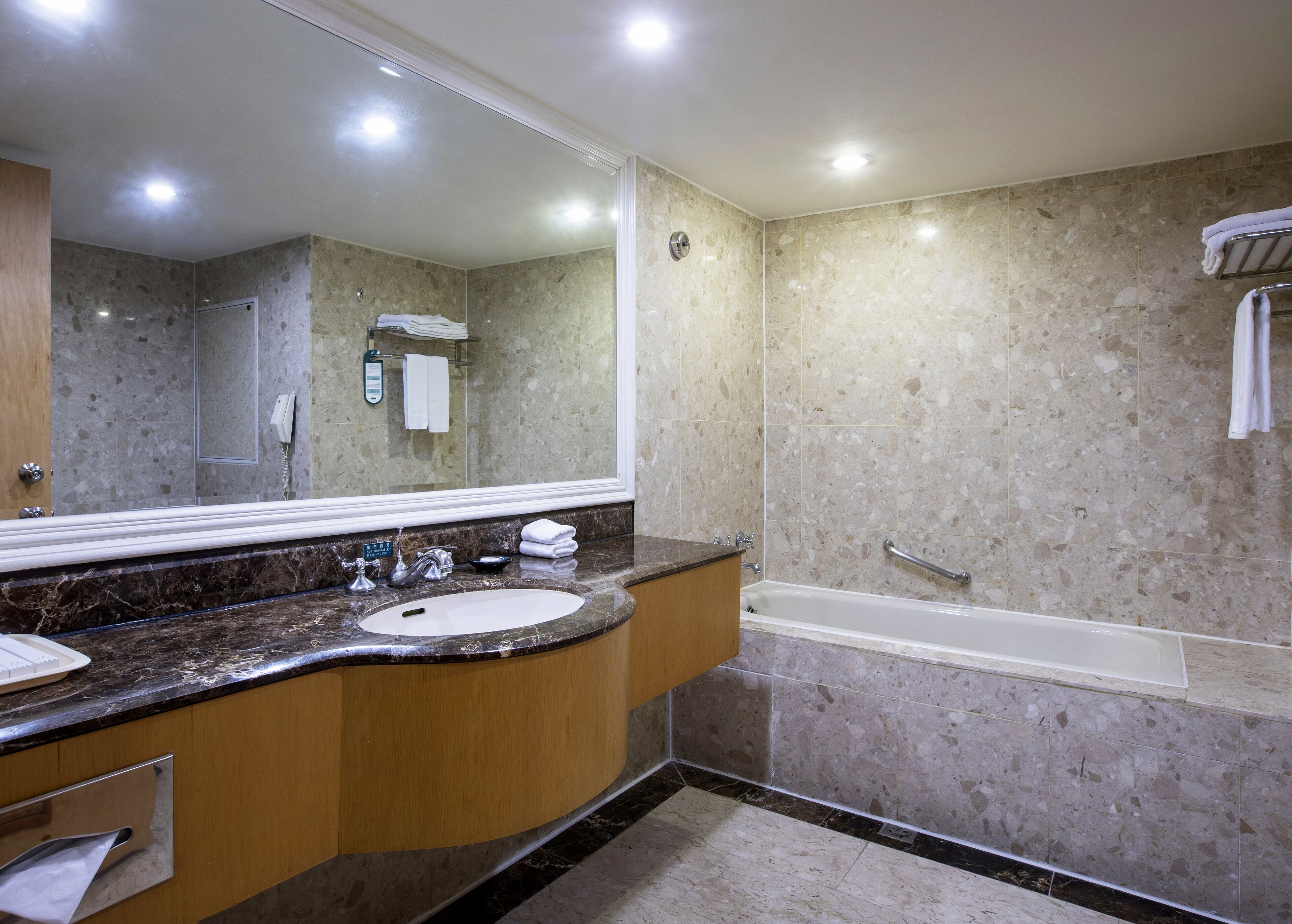 Een moderne badkamer met twee wastafels, een grote spiegel, een badkuip en marmeren wanden.