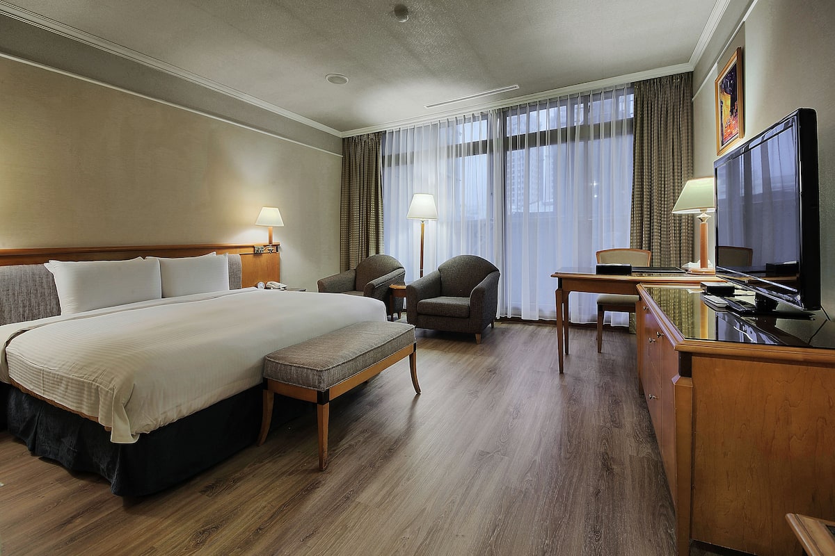 A hotel room with a large bed, a desk with a television, two armchairs, and a small table.