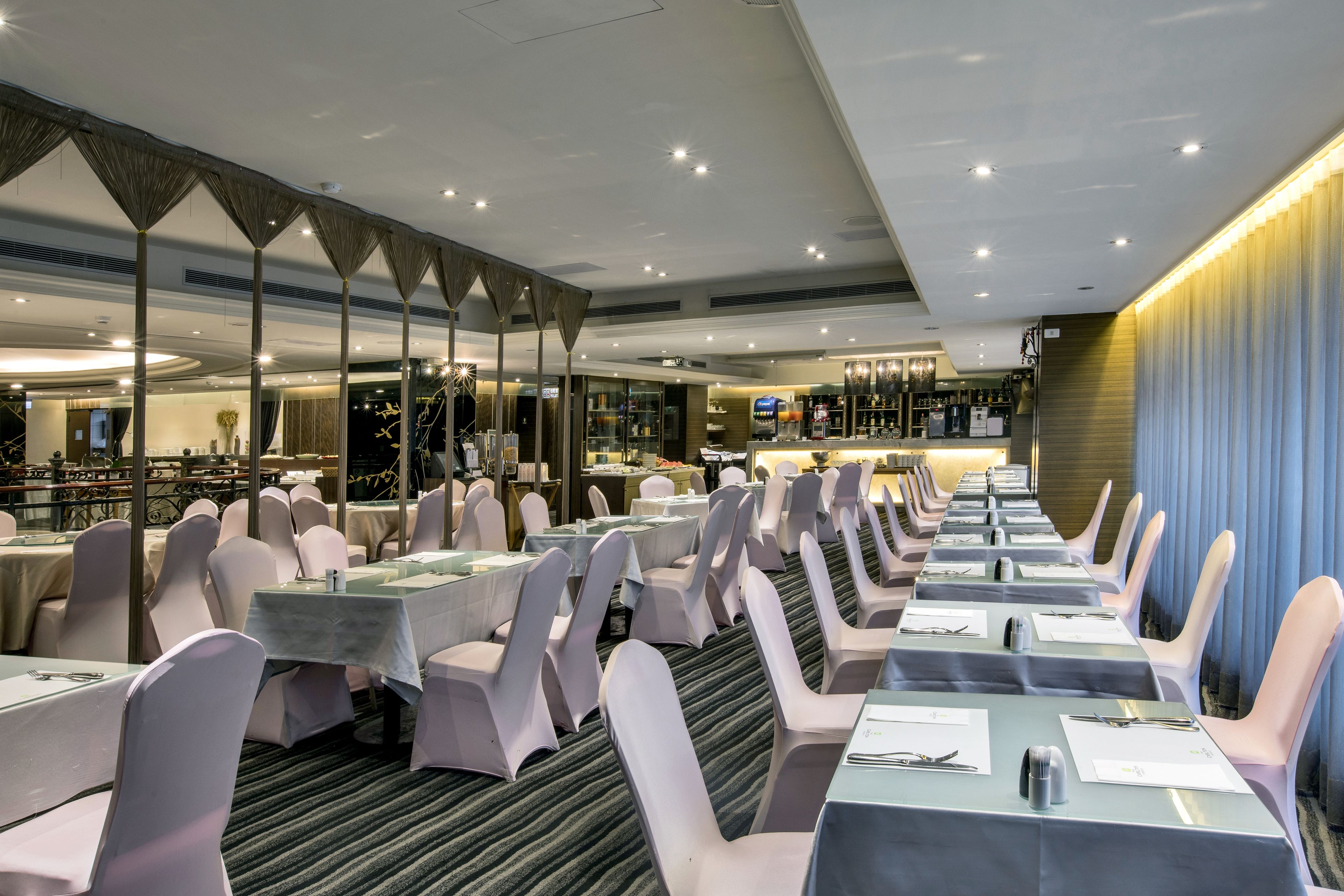 A banquet hall with rows of tables and chairs, a bar area, and a view of the restaurant in the background.