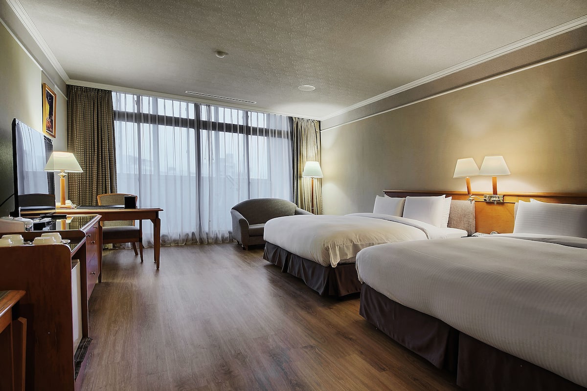 A hotel room with two beds, a desk, a chair, and a TV.