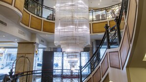 Interior de varios niveles con una escalera espiral central, una lámpara de araña colgante y vistas a la calle.