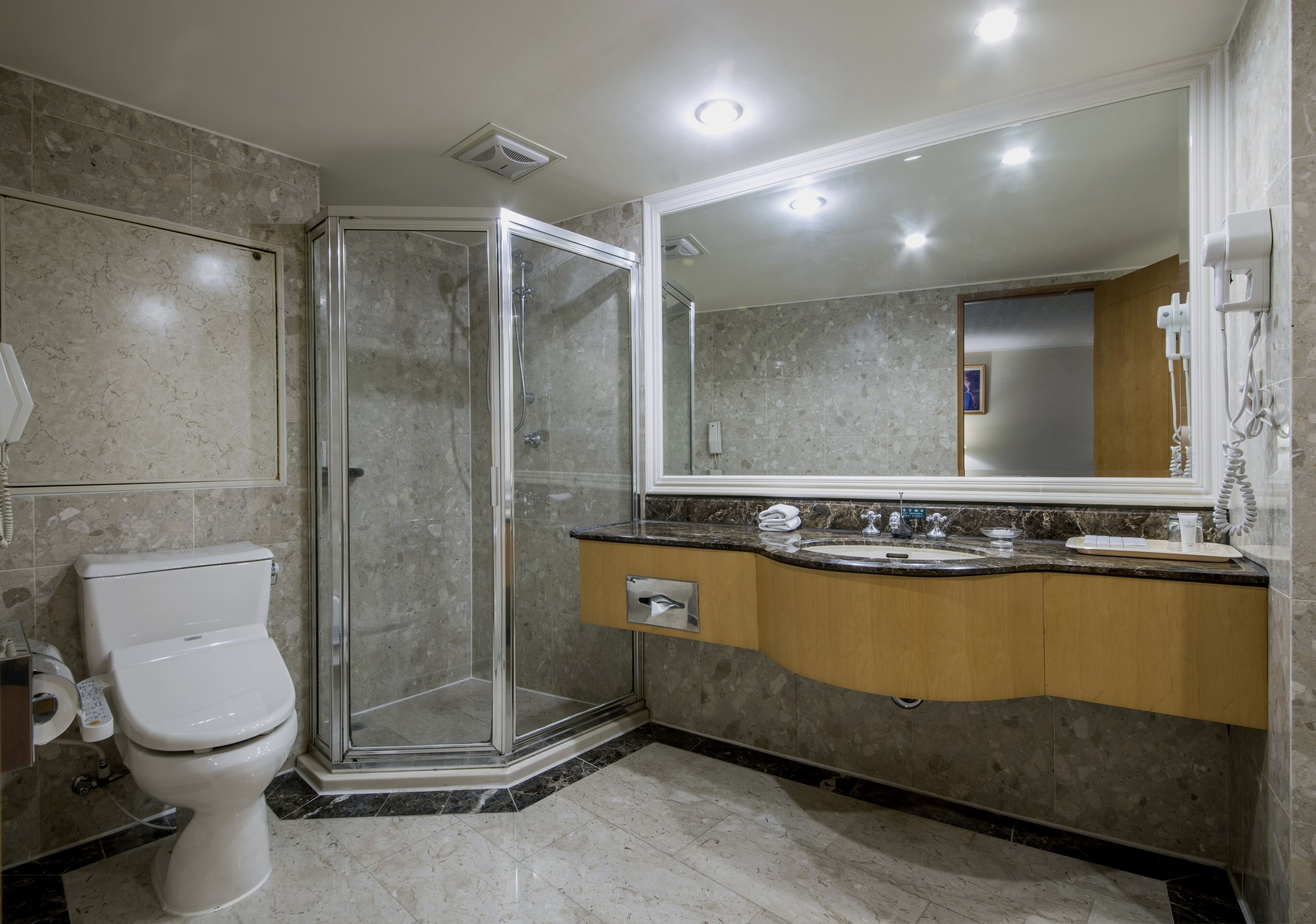 Un baño moderno con ducha de vidrio, inodoro, lavabo con tocador y un espejo grande.