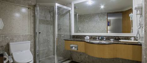 Un baño moderno con ducha de vidrio, inodoro, lavabo con tocador y un espejo grande.