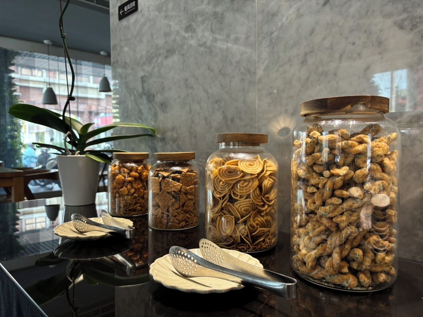 A kitchen counter with four glass jars containing different food items, a potted plant, and kitchen utensils.