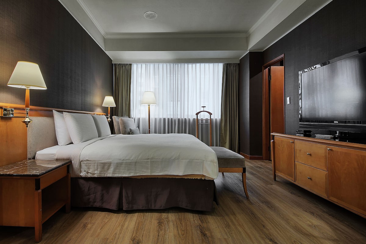 A hotel room with a large bed, bedside tables with lamps, a TV, and a wardrobe.