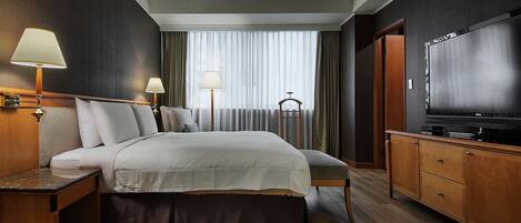 A hotel room with a large bed, bedside tables with lamps, a TV, and a wardrobe.