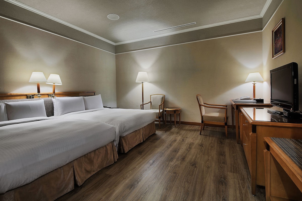 A hotel room with two beds, a desk, a chair, and a television.
