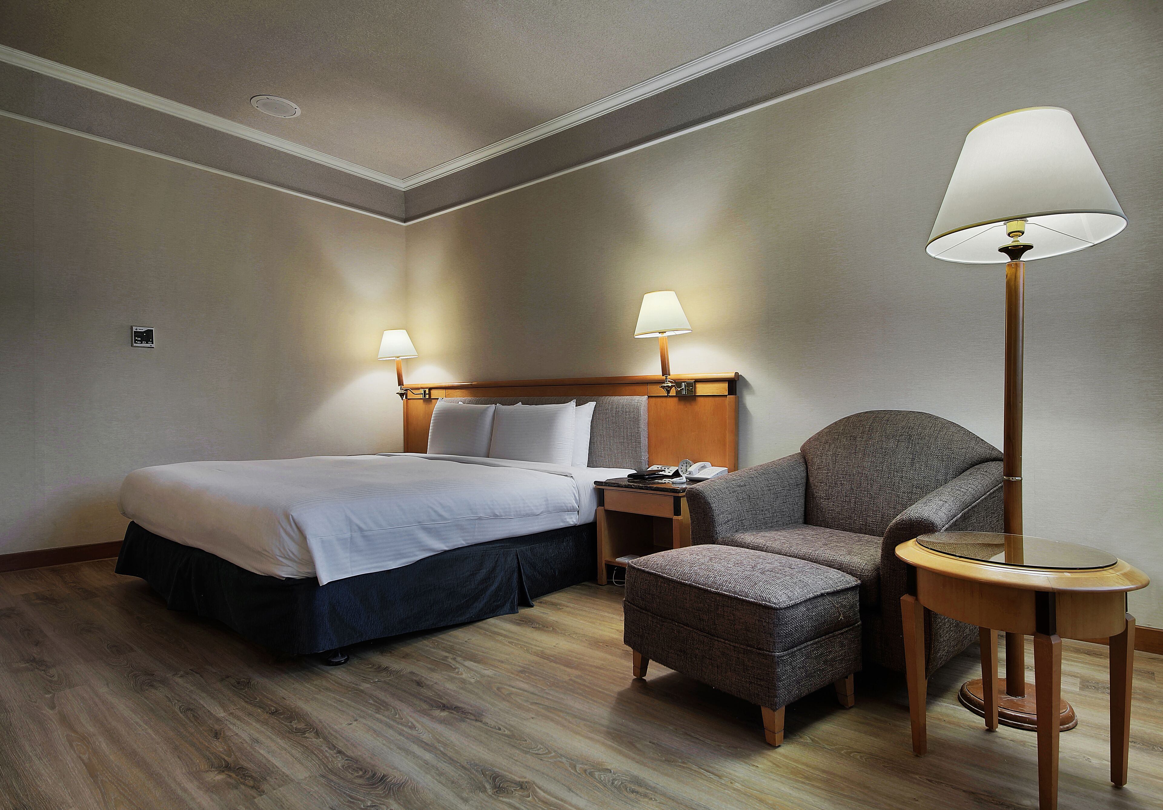 A hotel room with a bed, a chair, a small table, and two lamps.