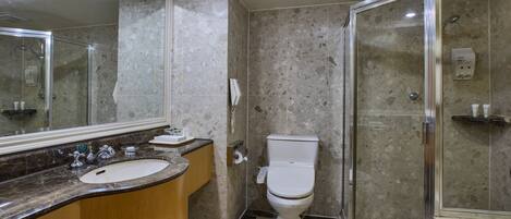 A modern bathroom with a marble sink, a toilet, and a glass-enclosed shower.