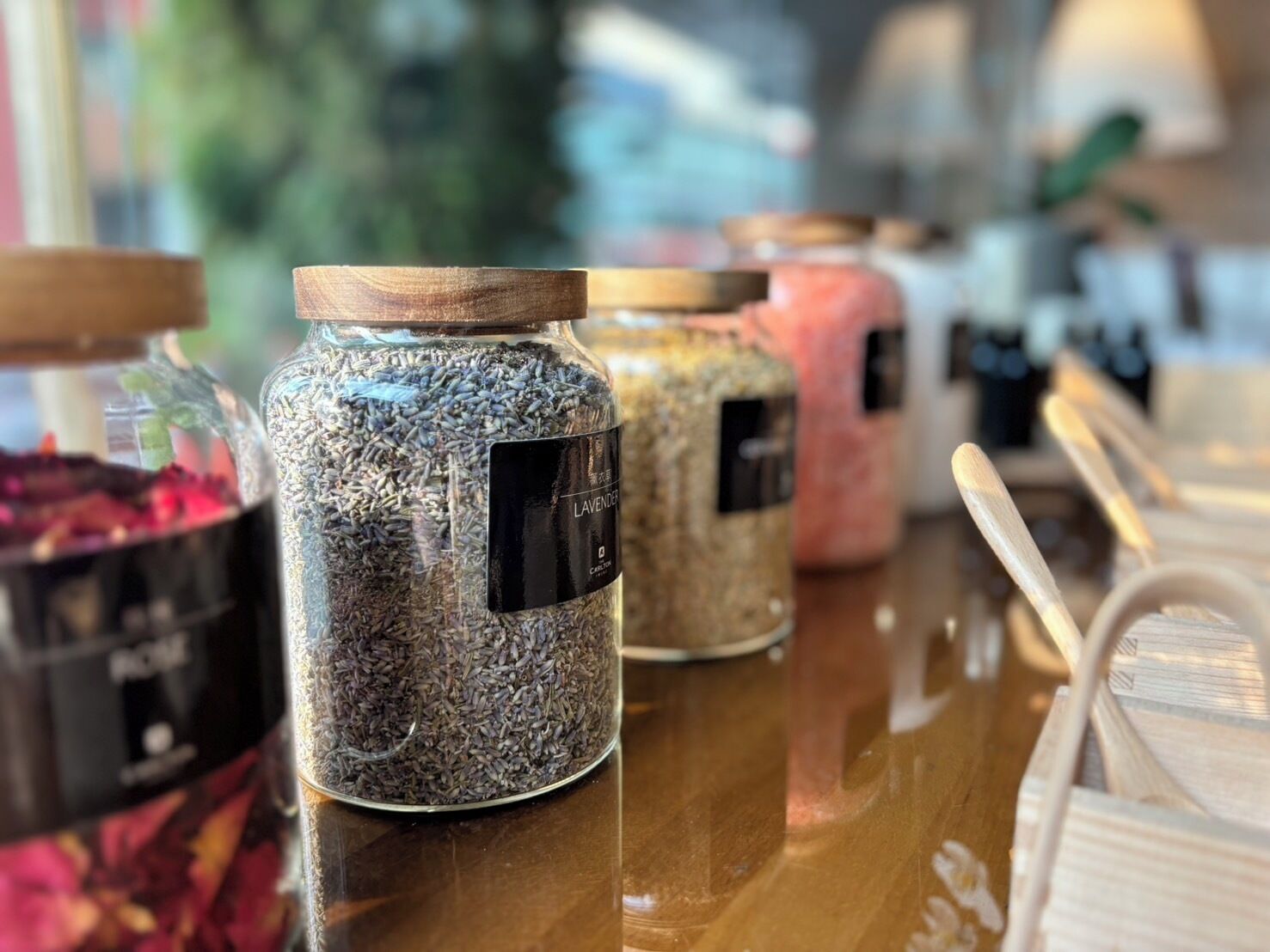 On peut voir une variété de bocaux étiquetés, disposés sur une surface en bois, et qui contiennent probablement différents types d’épices ou d’herbes aromatiques.