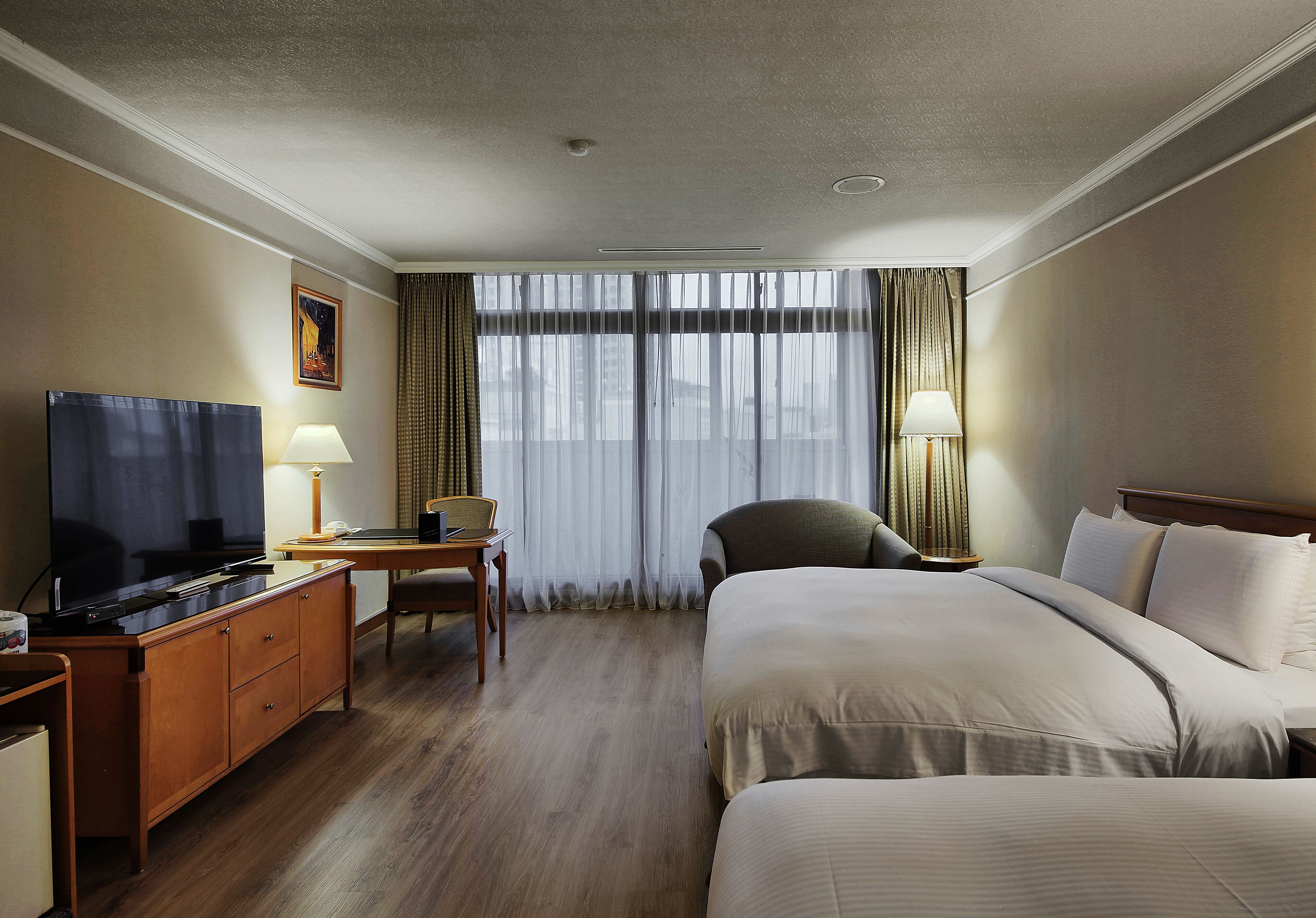 A hotel room with a large bed, a desk with a lamp, a television, and a chair.