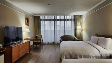 A hotel room with a large bed, a desk with a lamp, a television, and a chair.