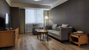 Habitación de hotel con un escritorio de madera, un sofá, una pequeña mesa redonda, una lámpara y un teléfono.