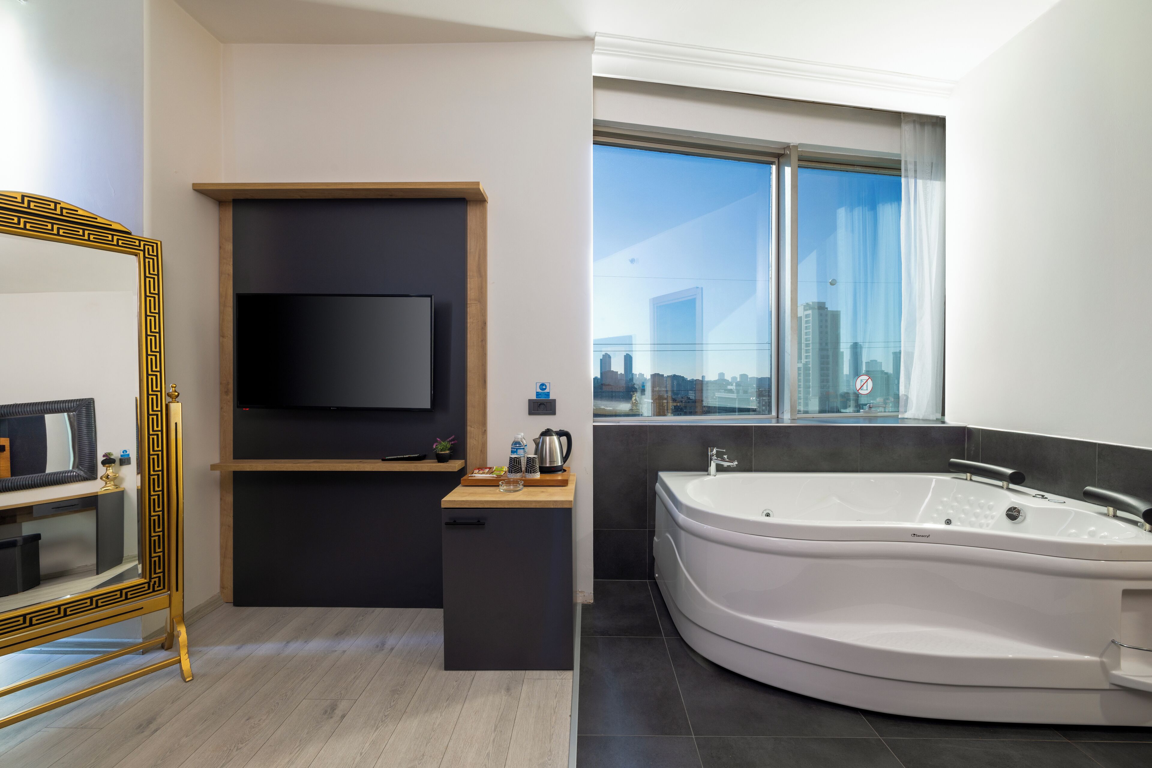 Une salle de bain moderne avec une grande baignoire, un téléviseur fixé sur un panneau en bois et une vue sur la ville à travers une grande fenêtre.