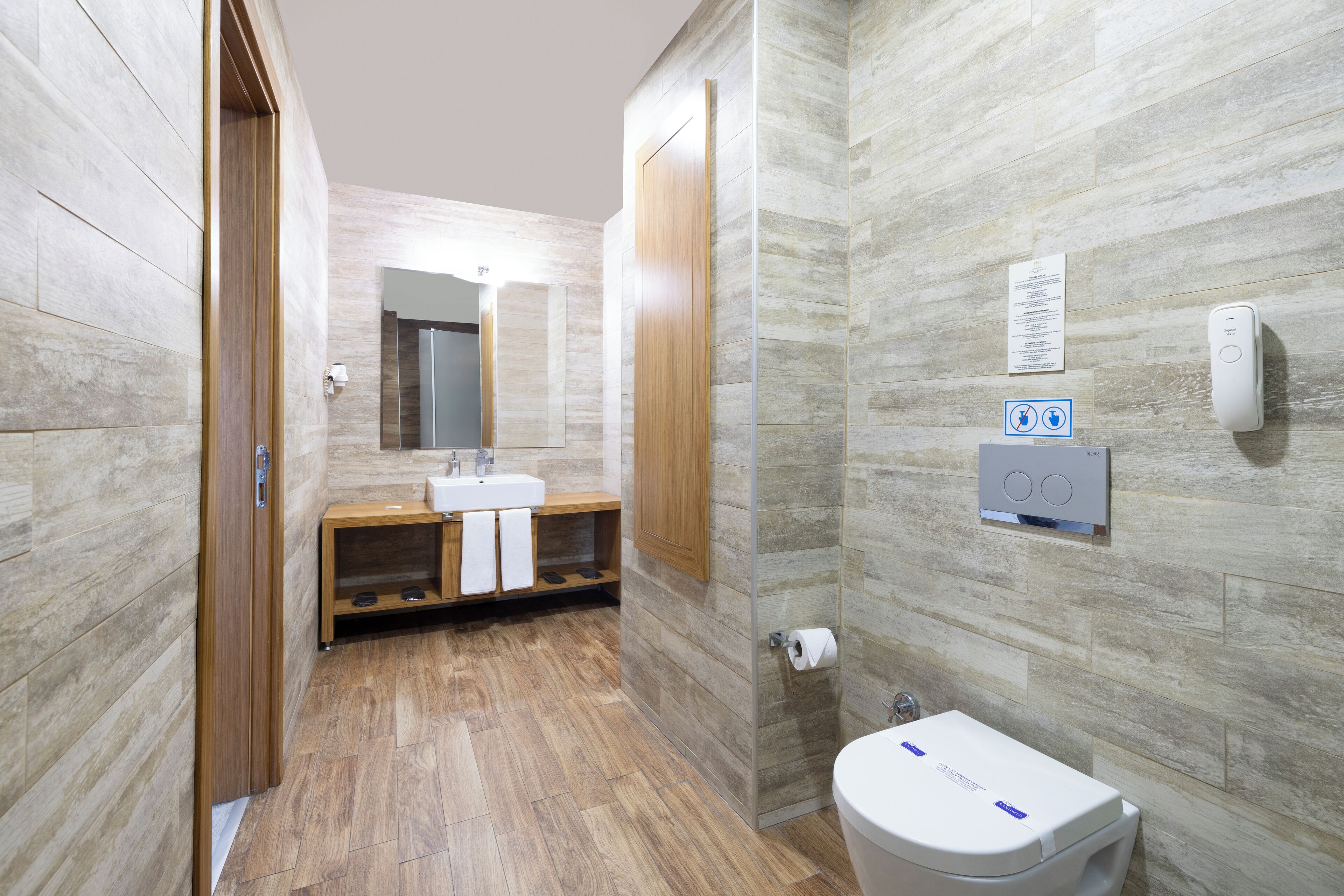 Une salle de bain moderne avec un meuble-lavabo en bois, un grand miroir, des toilettes et un sèche-mains fixé au mur.