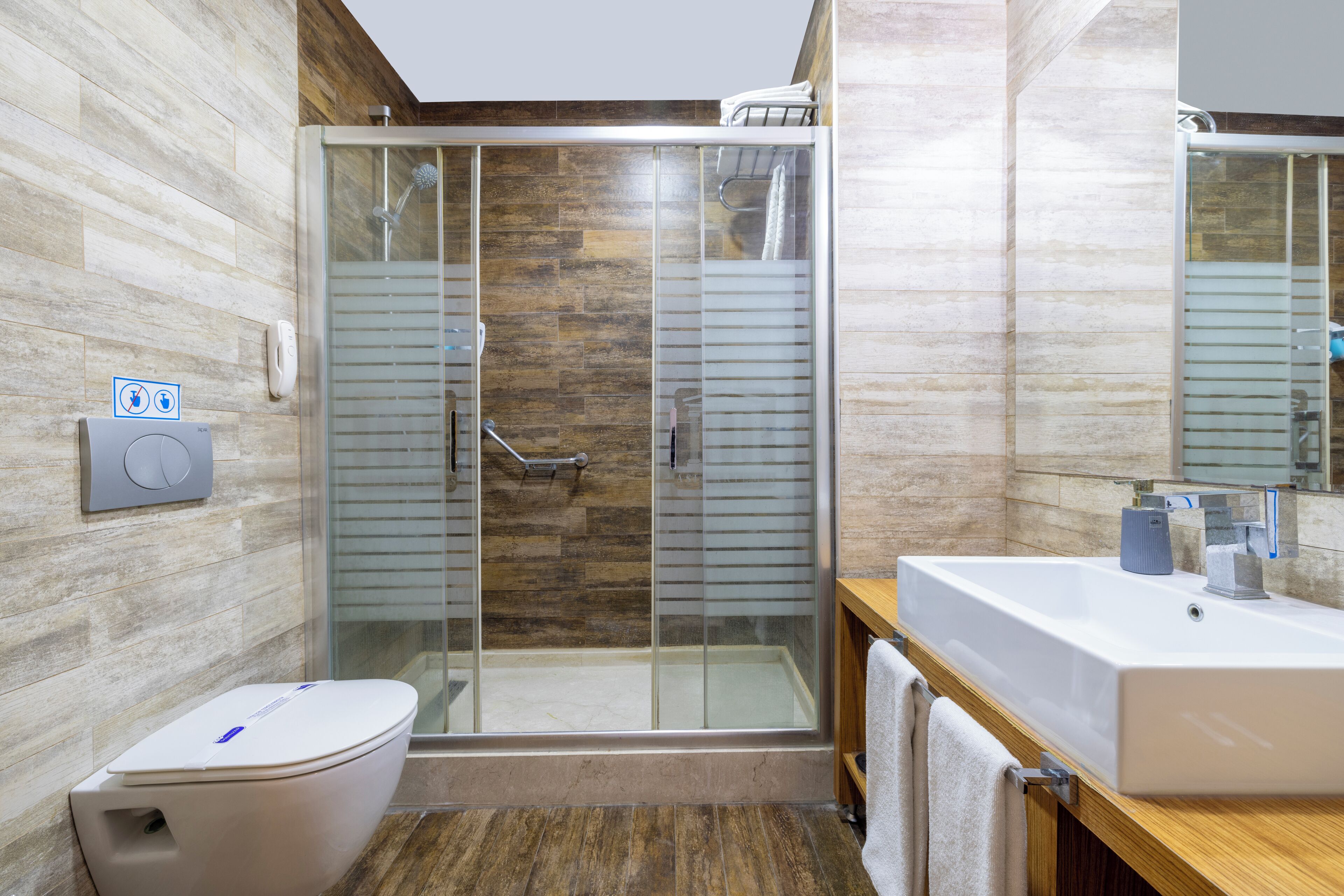 Une salle de bain moderne avec une douche à parois de verre, des toilettes blanches et un meuble-lavabo en bois avec un évier.