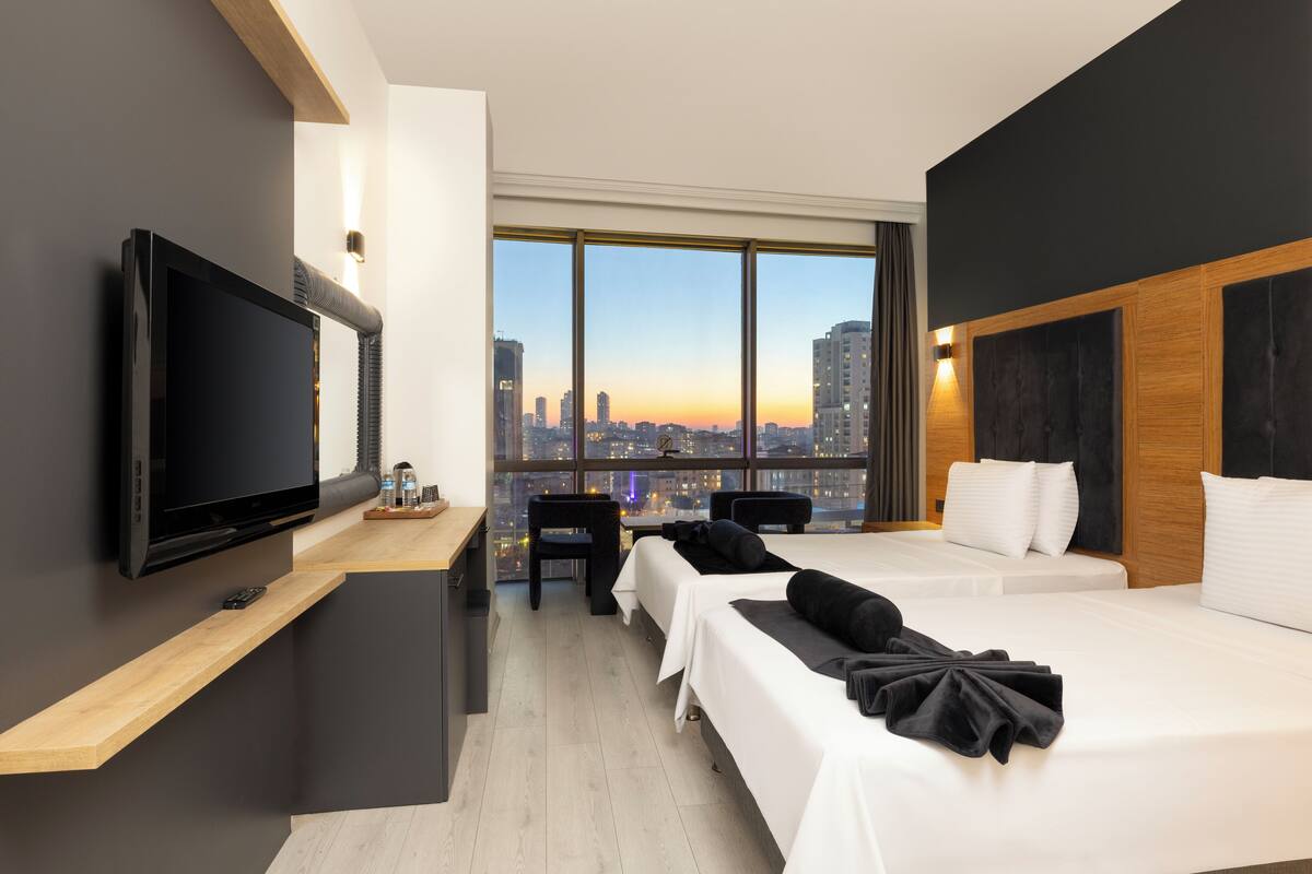 Una habitación de hotel moderna con un televisor grande, un escritorio, dos camas, vistas a la ciudad y una pared de acento de madera.