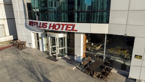 The exterior of MyPlus Hotel with a glass entrance, outdoor seating area, and a clear view of the interior through the windows.