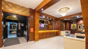 A hotel lobby with a reception desk, a sofa, a chandelier, and a television screen.