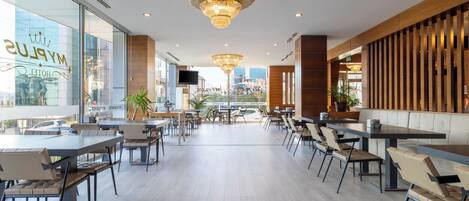 A modern hotel lobby with a chandelier, seating areas, and large windows.