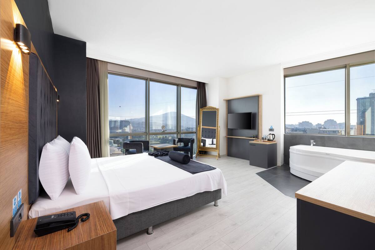 Una habitación de hotel moderna con una cama grande, un escritorio, un sofá, un televisor y una bañera.