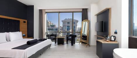 Une chambre d’hôtel moderne avec un grand lit, un bureau doté d’un téléviseur à écran plat, une petite table et une chaise. Une grande fenêtre offre une vue sur la ville.