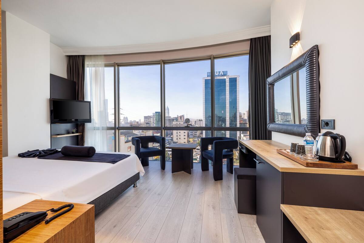 Una habitación de hotel moderna con una cama grande, un escritorio, una silla, un televisor y vistas a la ciudad.