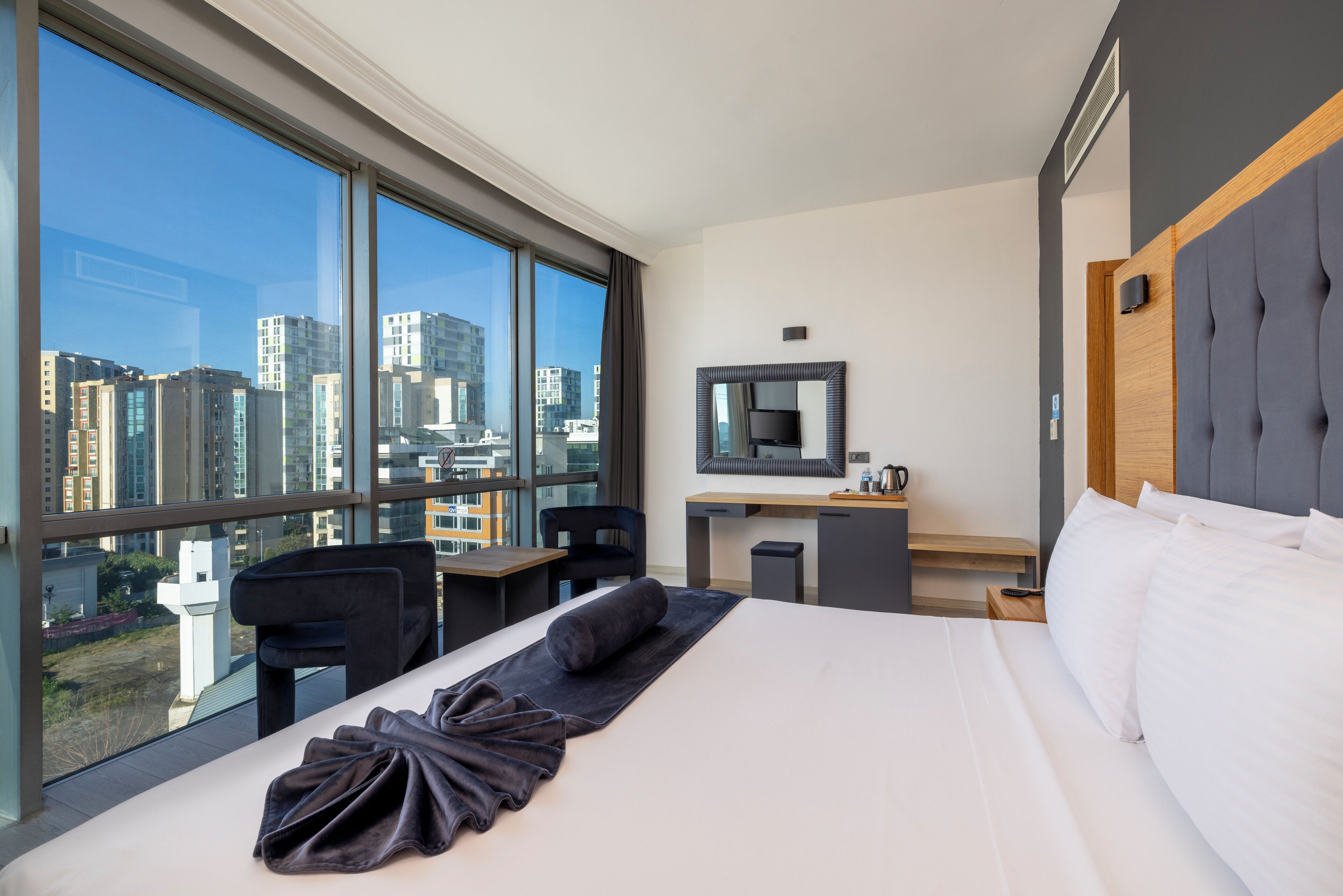 A hotel room with a large window, a bed, a desk, and a chair.