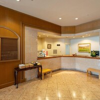 Zona de recepción de hotel con mostrador, banco y un cuadro en la pared.
