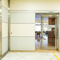 Entrada de hotel con puerta de vidrio, piso de baldosas y un interior visible con mobiliario.