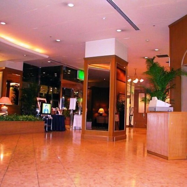 Un vestíbulo de hotel con una recepción, un letrero de salida verde y un área de recepción con una mesa y sillas.