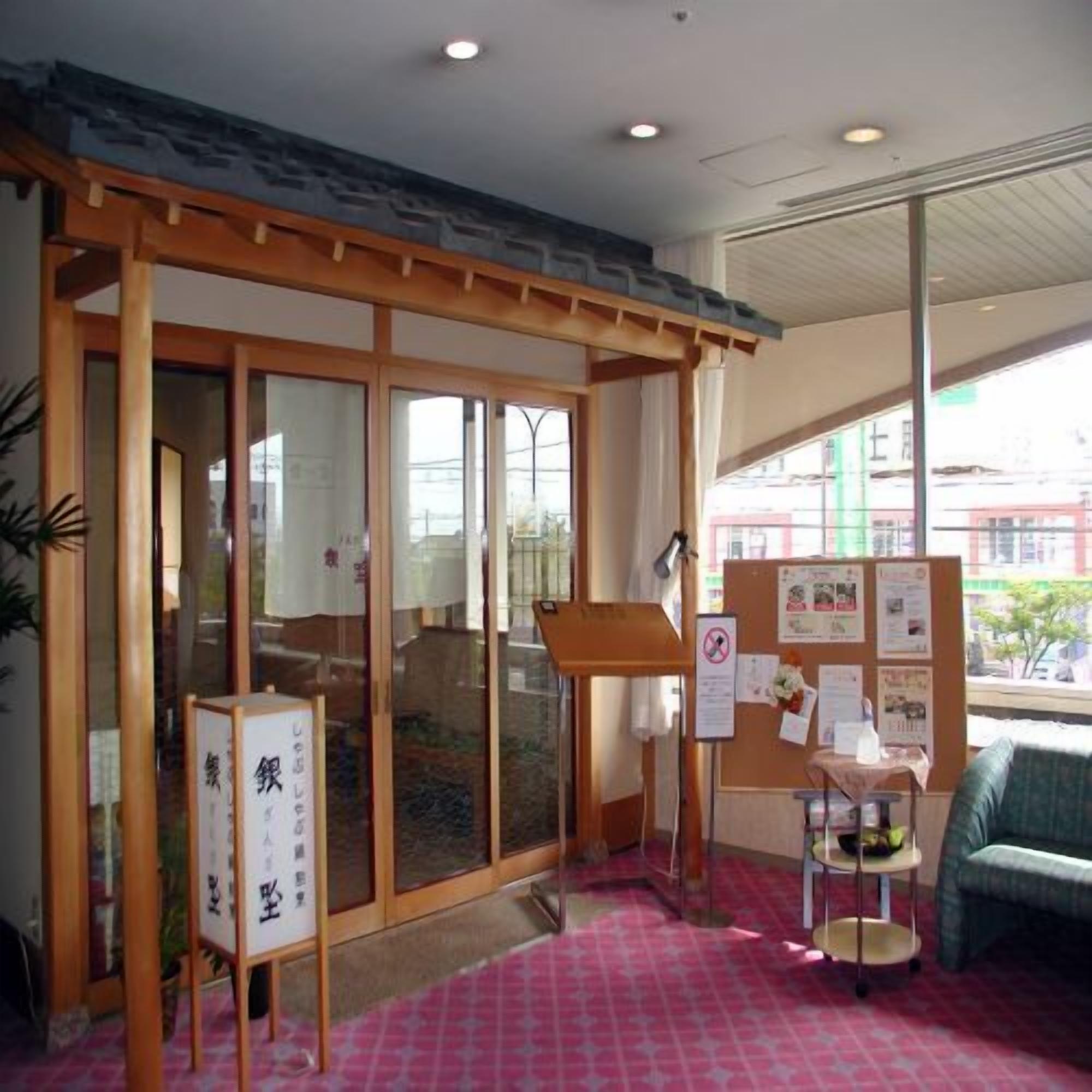 A room with a sliding glass door, a bulletin board with notices, a small table with a chair, and a pink patterned carpet.
