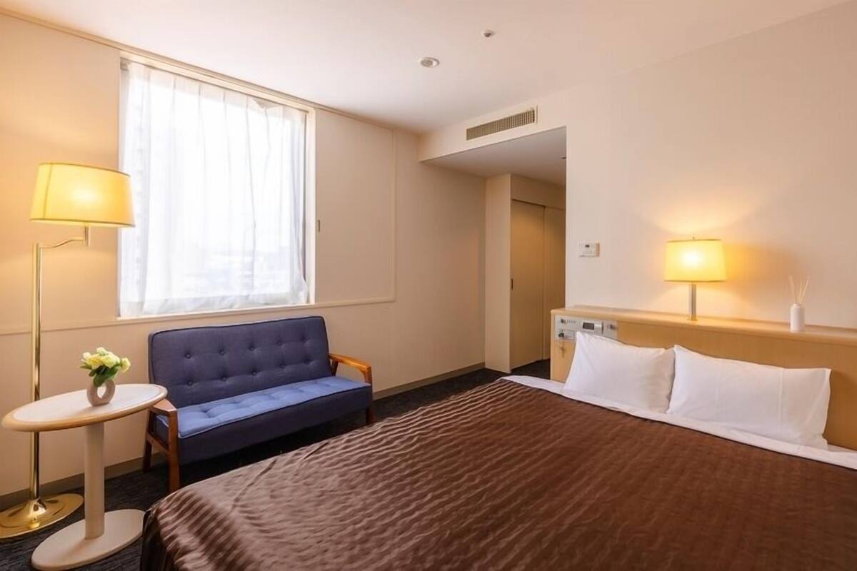 Ein Hotelzimmer mit Bett, Sofa, einem kleinen Tisch mit Lampe und einem Fenster mit Vorhängen.
