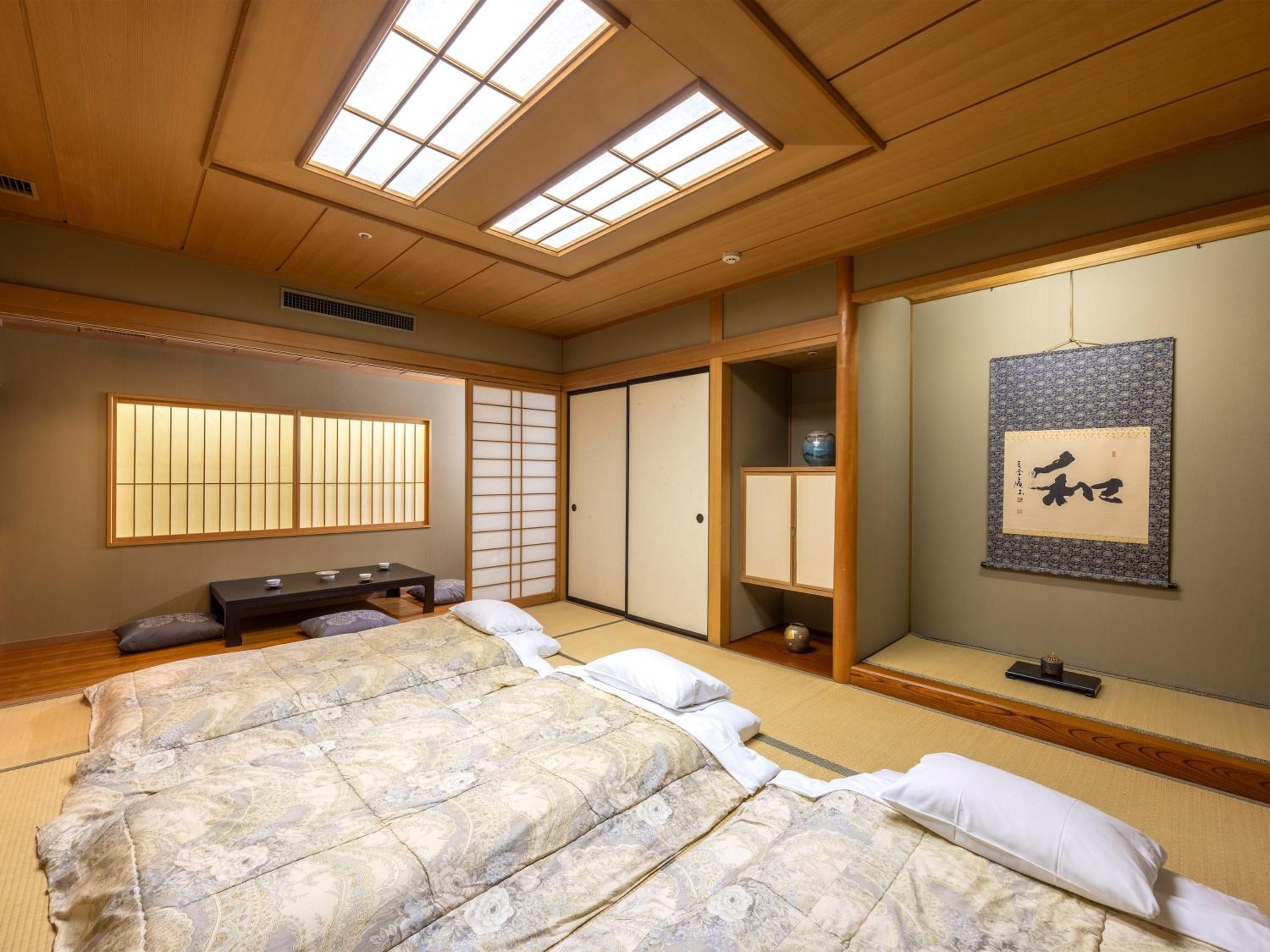 Un dormitorio de estilo japonés tradicional con suelo de tatami, cama con ropa de cama estampada con motivos florales, puertas correderas y un panel shoji.