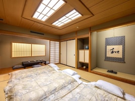 Un dormitorio de estilo japonés tradicional con suelo de tatami, cama con ropa de cama estampada con motivos florales, puertas correderas y un panel shoji.