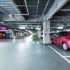 Useita kerroksia sisältävä pysäköintihalli, jossa on betonipilarit, opasteet ja muutama parkissa oleva auto.