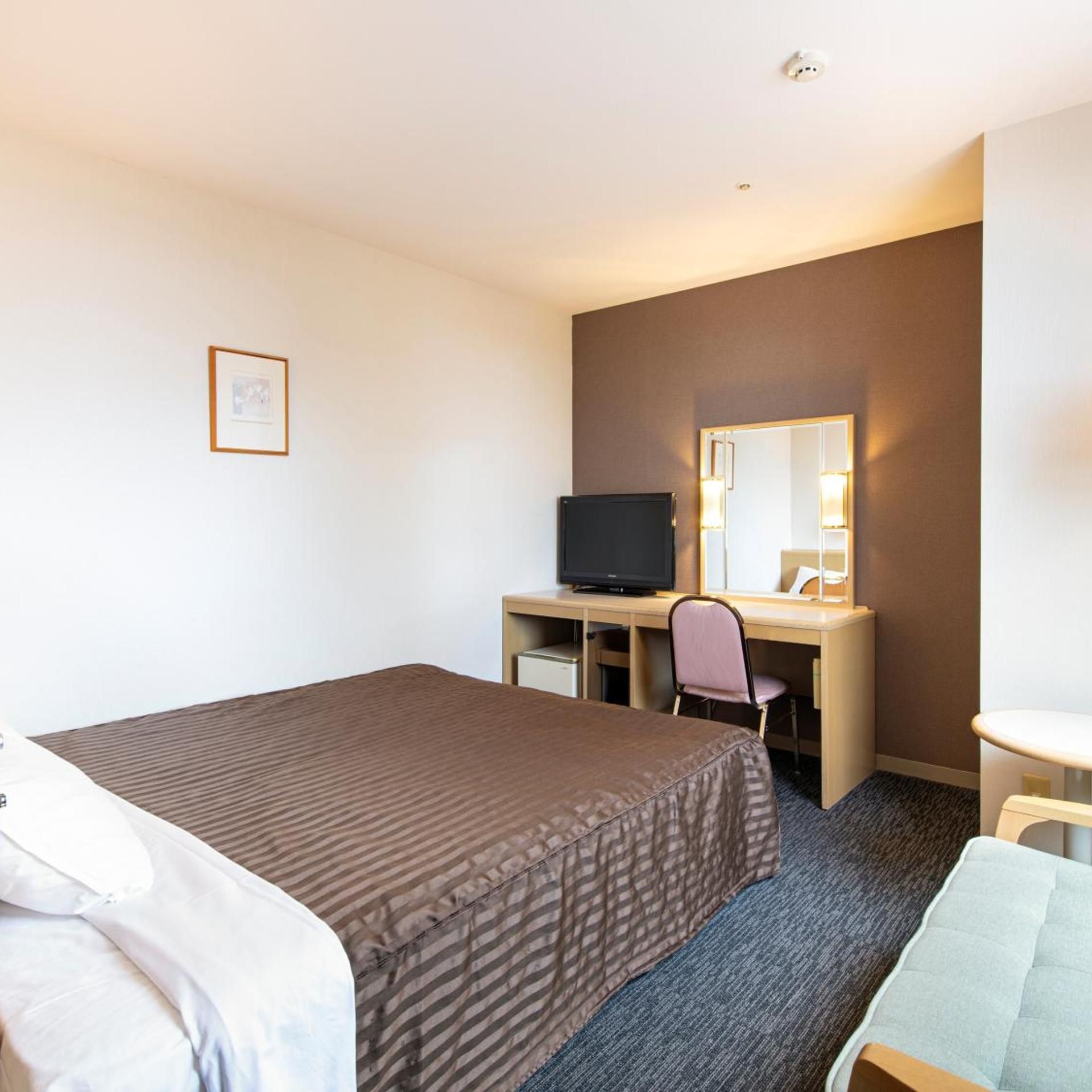 Une chambre d’hôtel comprenant un lit, un bureau avec un ordinateur et une télévision, une chaise, une petite table et un miroir.