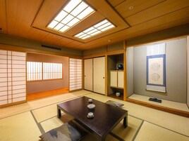Una habitación japonesa tradicional con suelo de tatami, una mesa de madera baja con juegos de té, puertas correderas y un pergamino colgado en la pared.
