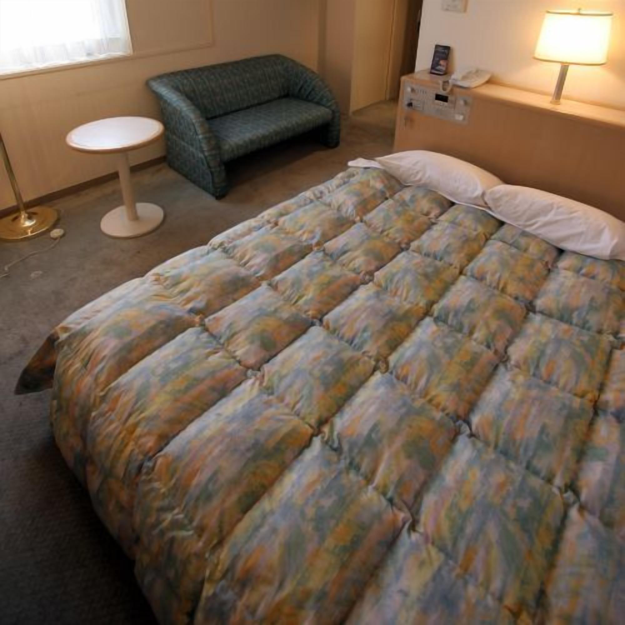 A bedroom with a bed, a chair, a bedside table, and a lamp.
