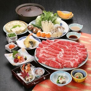Variedad de platos japoneses, incluyendo sashimi, verduras y carne, sobre una mesa.