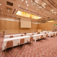 Un salón de conferencias con varias mesas, sillas y una pantalla de presentación.