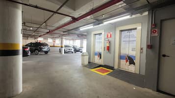 Un estacionamiento con varios automóviles, extintores e indicación de alarma contra incendios.