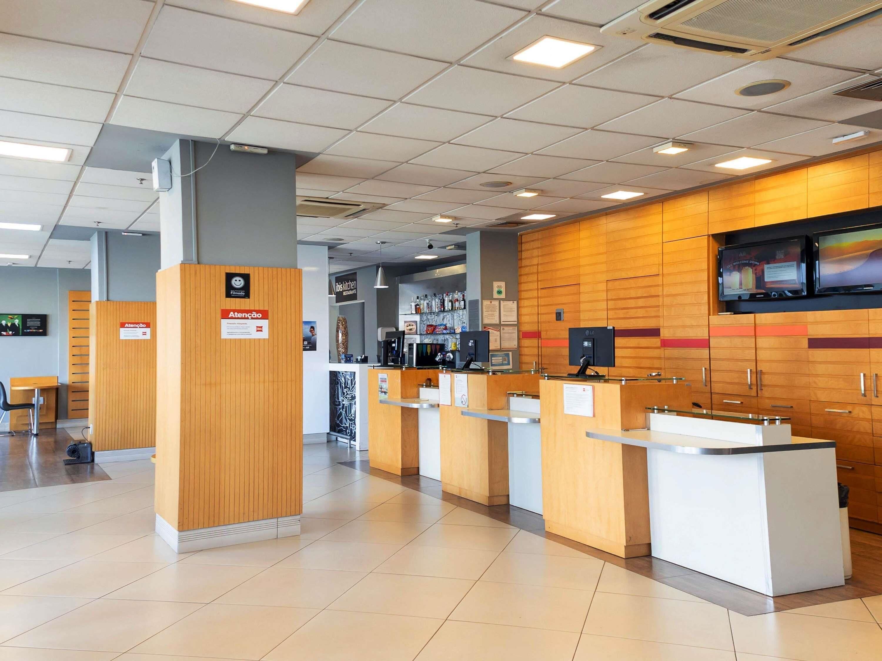 Un área de recepción con mostradores de madera, un panel informativo digital y suelo de baldosas.