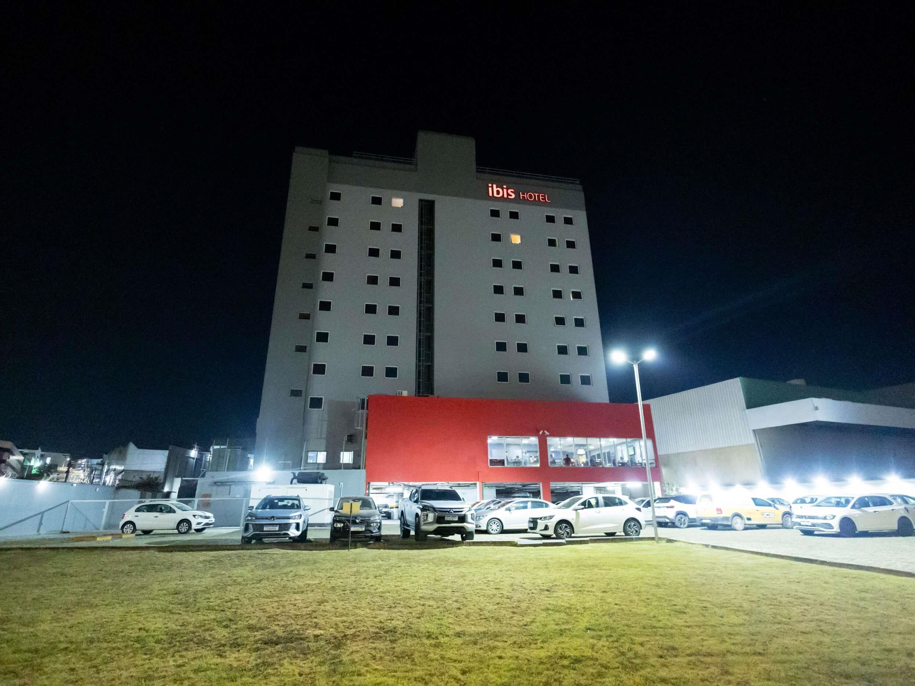 A hotel with a red and white facade, multiple parking spaces, and a tall building in the background.